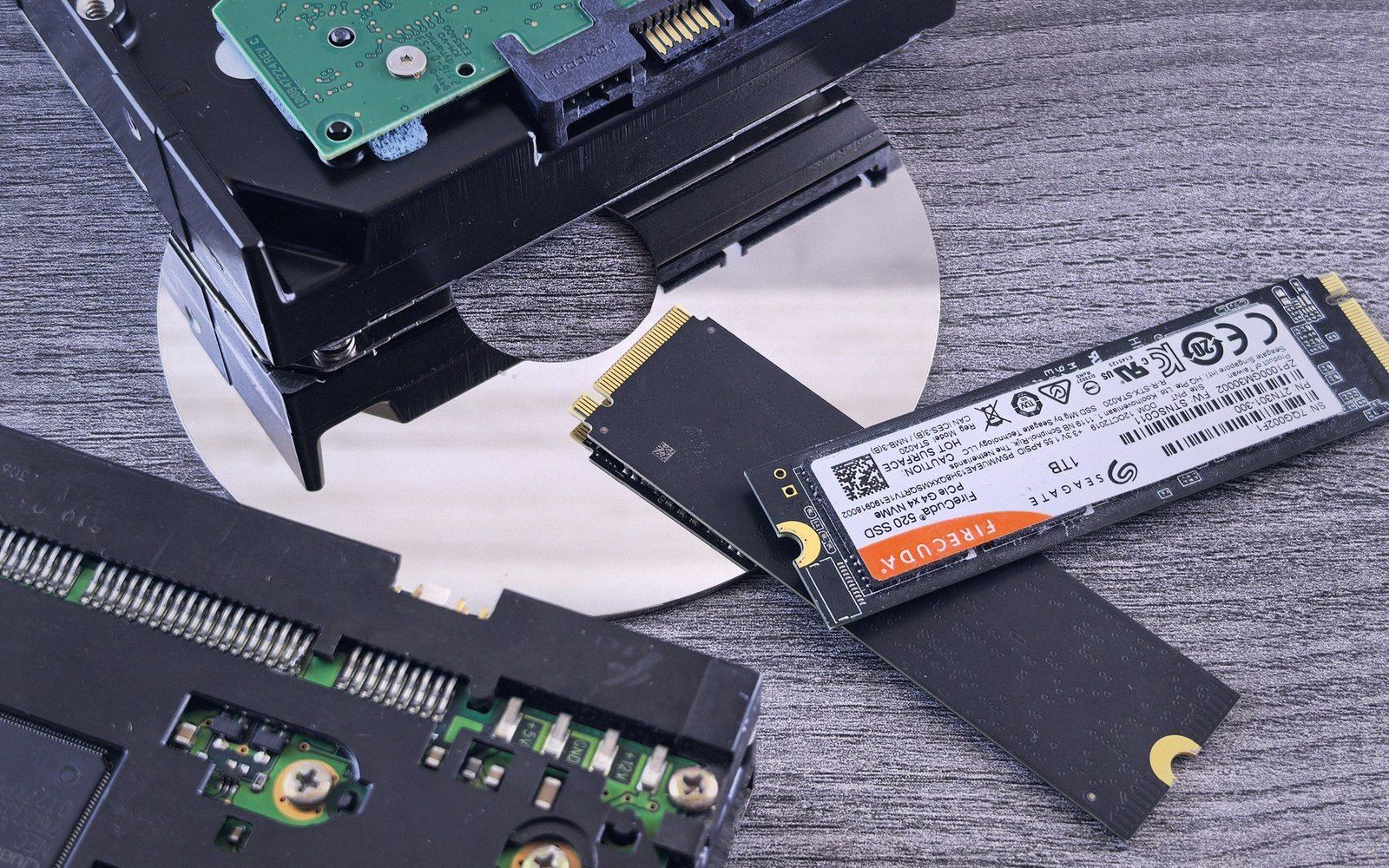An M.2 SSD lying atop a disassembled hard drive with its platter exposed