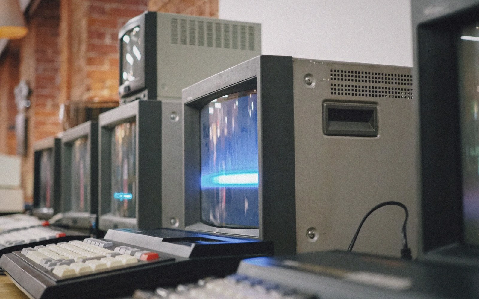 A row of vintage computer monitors with keyboards displaying glowing blue screen content