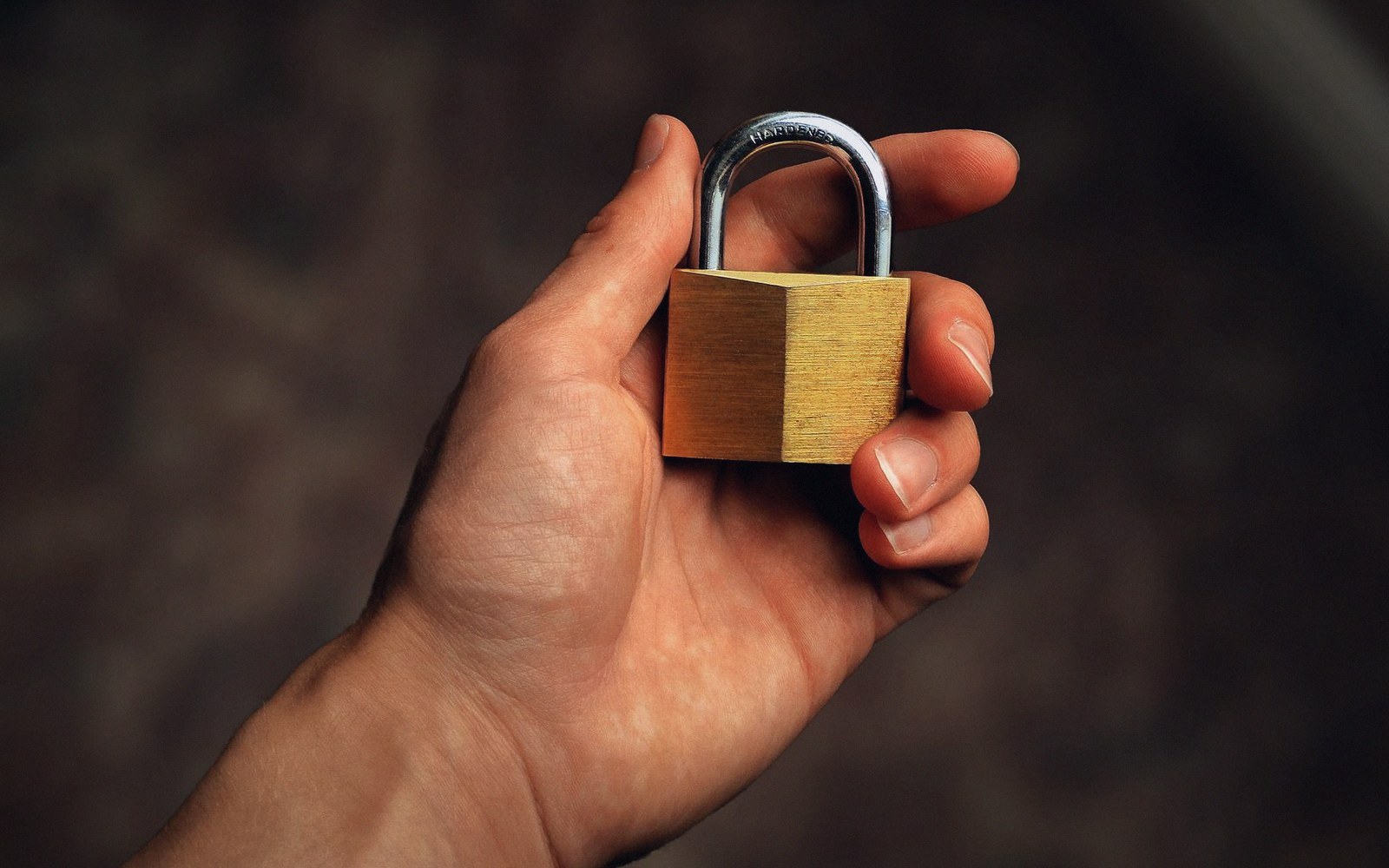 A hand holding a small open brass padlock by its shackle